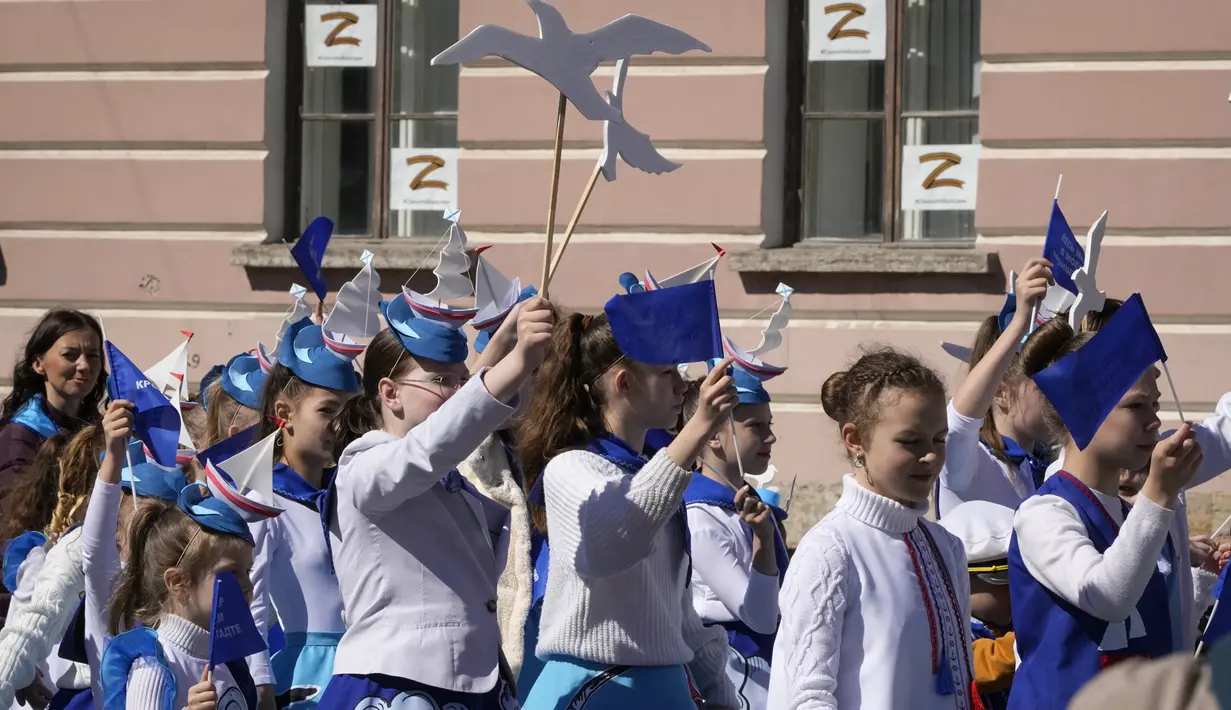 Anak-anak berbaris dengan latar belakang lembaran yang yang dipajang di jendela menggambarkan huruf Z simbol militer Rusia selama perayaan memperingati 318 tahun kota Kronstadt di luar St. Petersburg, Rusia (21/5/2022). (AP Photo/Dmitri Lovetsky)