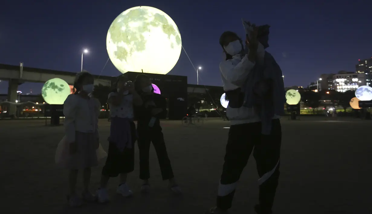 Warga berswafoto dekat instalasi bulan purnama yang bersinar di sebuah taman di Seoul, Korea Selatan, Jumat (18/9/2020). Pejabat setempat memasang bulan purnama buatan untuk meningkatkan semangat saat wabah COVID-19 sekaligus menyambut Chuseok, Thanksgiving versi Korea. (AP Photo/Ahn Young-joon)