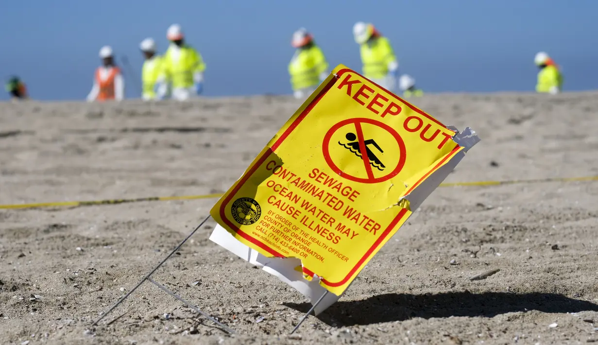 Sebuah tanda peringatan ditampilkan saat pekerja dengan pakaian pelindung membersihkan pantai yang terkontaminasi tumpahan minyak di Huntington Beach, California, Amerika Serikat, Selasa (5/10/2021). Kebocoran pipa menyebabkan tumpahan minyak di lepas pantai California. (AP Photo/Ringo H.W. Chiu)