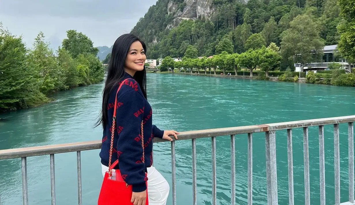 <p>Titi Kamal saat berpose di pinggir sungai di Swiss. Titi tampil cantik dengan rambut terurai dengan senyum yang bahagia dengan mengenakan Sweater biru dan membawa tas berwarna merah saat menikmati keindahan sungai tersebut. (instagram/titi_kamall)</p>