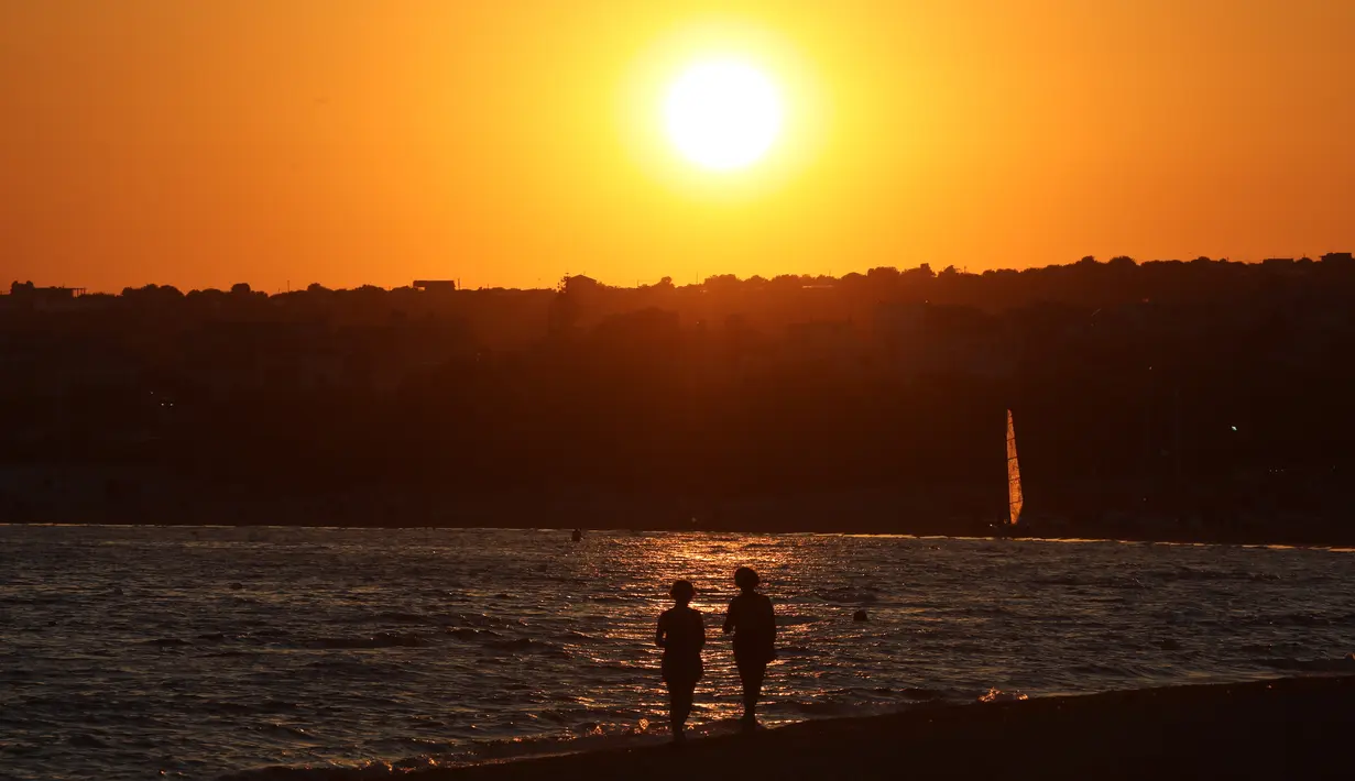 Sejumlah orang berjalan saat matahari terbenam di pantai Sampieri, Sisilia, (31/7). (AFP Photo/Ludovic Marin)
