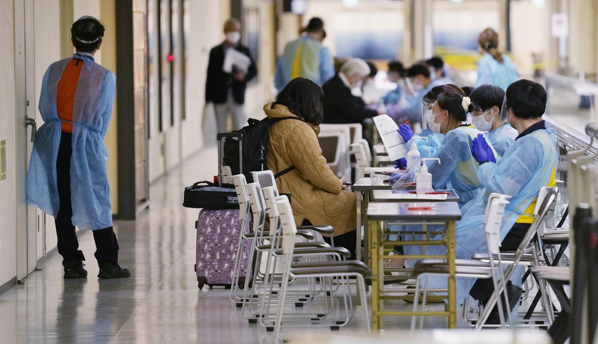 Anggota staf membantu penumpang menggunakan aplikasi ponsel untuk menjalani proses karantina pencegahan virus corona setelah mendarat di Bandara Internasional Narita di Narita, timur Tokyo, Jepang (2/12/2021). (AP Photo/Hiro Komae)