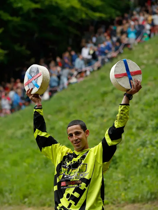 Chris Anderson berpose dengan keju yang dimenangkannya dalam kompetisi Cheese Rolling di Brockworth, Gloucestershire, Inggris, 30 Mei 2016. Peserta diharuskan mengejar keju berbentuk seperti roda yang digelindingkan dari puncak bukit. (Adrian DENNIS/AFP)
