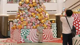 Pengunjung berfoto di depan pohon Natal yang menghiasi pusat perbelanjaan di kawasan Menteng, Jakarta, Minggu (23/12). Konsep dekorasi pohon Natal modern disajikan untuk membuat suasana berbeda dari tahun-tahun sebelumnya. (Liputan6.com/Herman Zakharia)