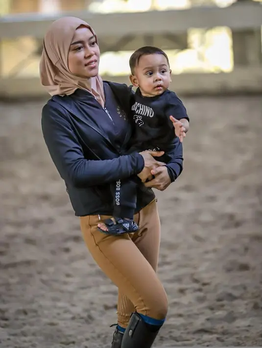 Lesty terlihat memasukkan hijabnya ke dalam jaket hoodie. Agar tetap leluasa saat berkuda atau menggendong Baby L seperti foto ini. [Foto: @lestykejora]