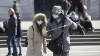 Suami istri bersiap selfie di kota Duomo, Milan, Italia, Kamis (27/2/2020). Kementerian Kesehatan Italia, hingga Rabu 4 Maret, mencatat ada 3.089 orang yang terinfeksi Virus Corona COVID-19. Rinciannya, 2.706 kasus positif, 107 orang meninggal dunia, dan 276 orang sembuh. (AP Photo/Luca Bruno)