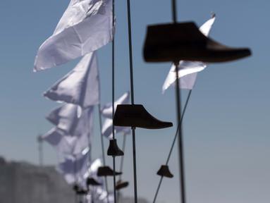 Sejumlah cetakan kayu sepatu dengan bendera putih yang merupakan seni instalasi di pajang di Playas de Tijuana, Meksiko (7/10). Seni instalasi yang bercerita tentang migran Meksiko ini adalah karya seniman Betsabee Romero. (AFP Photo/Guillermo Arias)