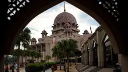 Gambar yang diambil pada 22 November 2017, menunjukkan wisatawan berjalan di sekitar Masjid Pink di kawasan Putrajaya, Malaysia. Selain warna yang unik, masjid ini juga dilengkapi dengan kubah berisikan lukisan dan kaligrafi indah. (MANAN VATSYAYANA/AFP)