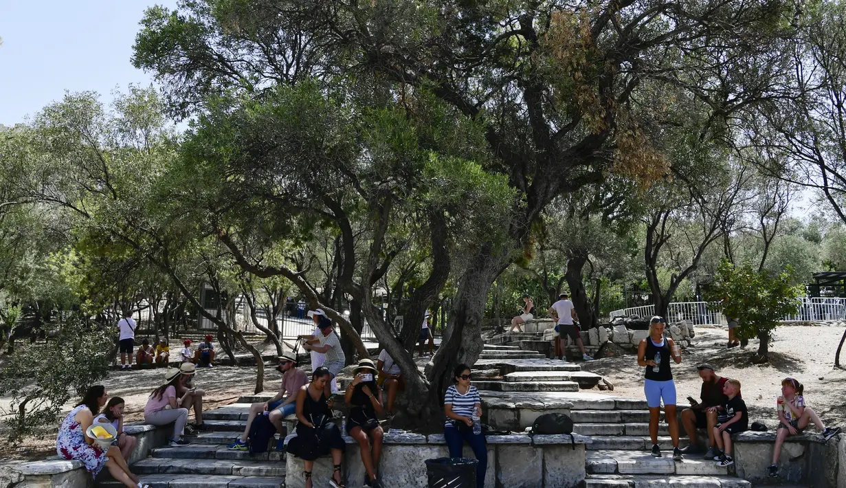 Turis duduk di bawah naungan di luar Acropolis kuno, di Athena Yunani (3/8/2021). Suhu mencapai 42 C (107,6 F) di beberapa bagian ibu kota Yunani, karena cuaca ekstrem memicu kebakaran hutan yang mematikan di Turki dan berkobar di seluruh wilayah. (AP Photo/Michael Varaklas)