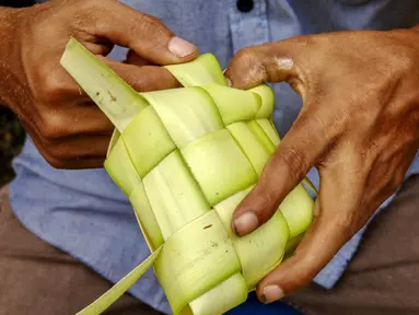 Seorang penjual menganyam daun kelapa atau kulit ketupat sambil menunggu pelanggan di sebuah pasar tradisional di Jakarta pada 2 April 2024. (BAY ISMOYO/AFP)