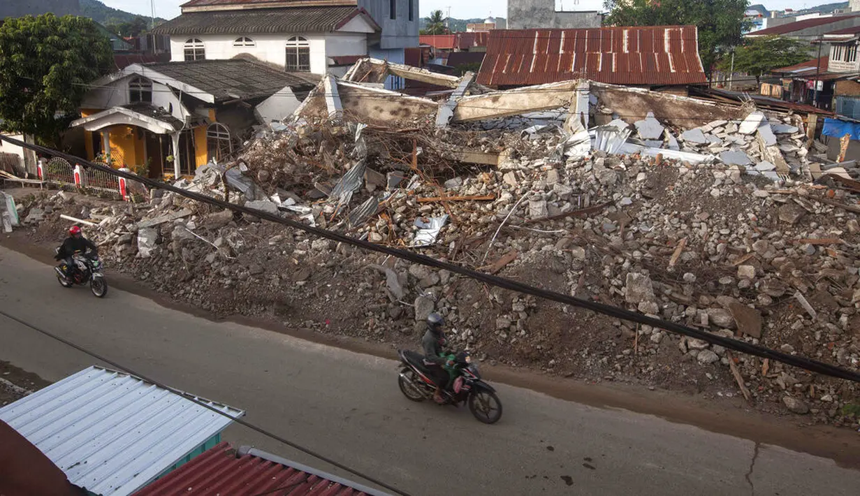 Pengendara sepeda motor melewati gedung-gedung yang runtuh akibat gempa di Mamuju, Sulawesi Barat, Indonesia, Senin (18/1/2021). Gempa Sulawesi Barat mengakibatkan 70 orang meninggal dunia di Kabupaten Mamuju dan 11 orang di Kabupaten Majene. (AP Photo/Yusuf Wahil)
