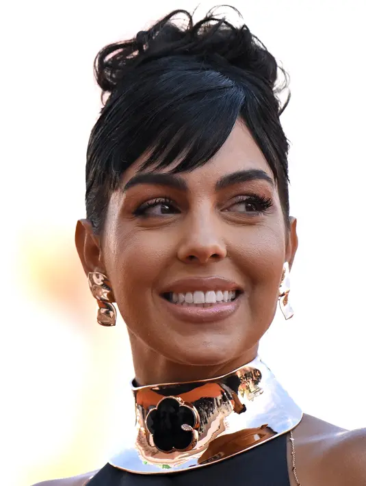 <p>Georgina Rodriguez tersenyum sambil berpose untuk fotografer setibanya di pemutaran perdana film 'Tar' selama Venice Film Festival ke-79 di Venesia, Italia (1/9/2022). Georgina memakai palet riasan perunggu sempurna dengan lipstik natural di bibirnya. (AFP/Tiziana Fabi)</p>
