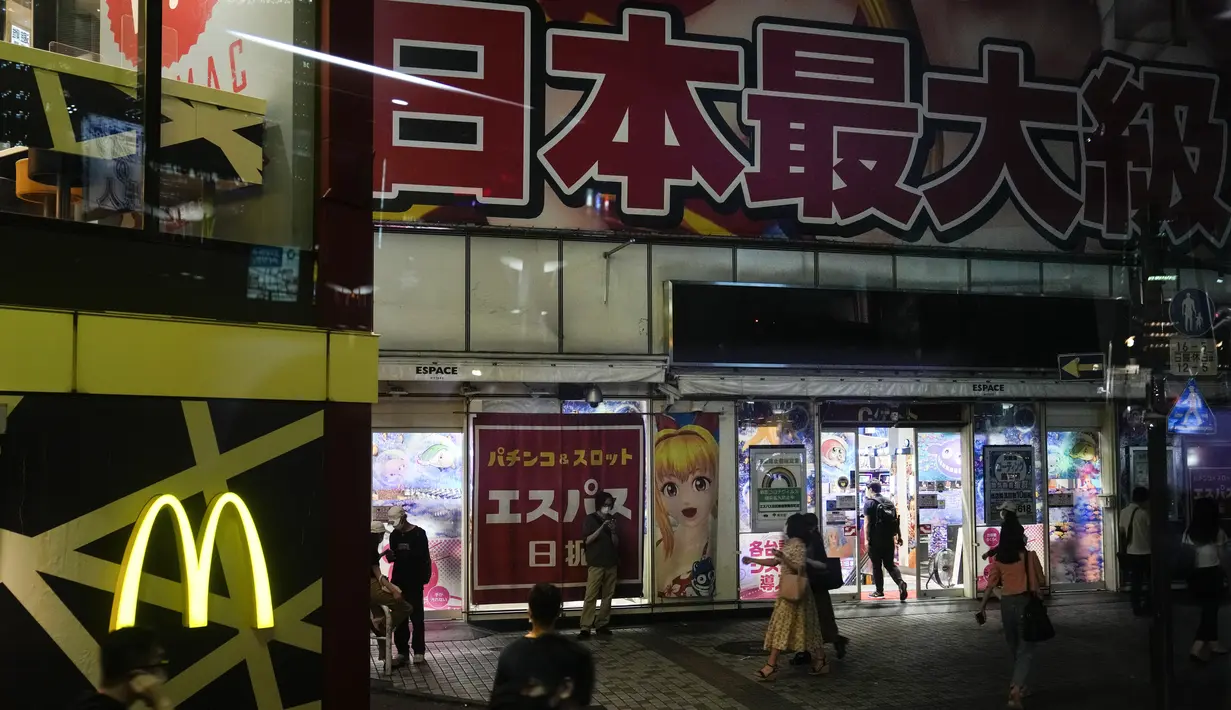 Orang-orang berjalan di dekat ruang pachinko menjelang Olimpiade Musim Panas 2020 di Tokyo pada 13 Juli 2021. Di bawah protokol yang ketat, satu-satunya cara untuk melihat sekilas ibu kota adalah dari kendaraan yang mengantar para tamu dari perkampungan atlet atau hotel ke venue (AP Photo/Jae CHong)