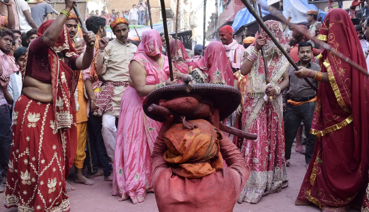 Sejumlah perempuan India memukulkan tongkat ke arah tameng yang dipegang seorang pria selama perayaan Lathmar Holi di Barsana, Uttar Pradesh, India (6/3). Lathmar sendiri berarti memukul dengan tongkat. (AFP Photo/STR)