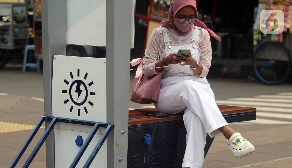Seorang perempuan mengisi ulang daya ponsel pada stasiun Pengisian Listrik Bertenaga Surya atau Solar Charging Station di kawasan Transit Oriented Development (TOD) I Dukuh Atas, Jakarta, Rabu (10/11/2022). Adapun lokasi pengisian daya ini mempunyai kapasitas maksimal 500 watt. (Liputan6.com/Johan Tallo)