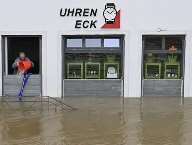 Seorang pria mencoba menumpahkan air dengan ember dari toko arlojinya di jalan dan rumah-rumah yang tergenang banjir di pusat kota Passau, Bavaria, wilayah selatan Jerman, pada 4 Juni 2024. (Michaela STACHE/AFP)