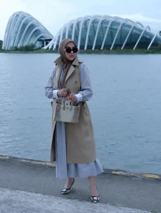 Striped shirt maxi dress jadi terlihat lebih chic saat Syahrini memadukannya dengan sleeveless coat dan tas Hermes warna beige senada. [@princessyahrini]