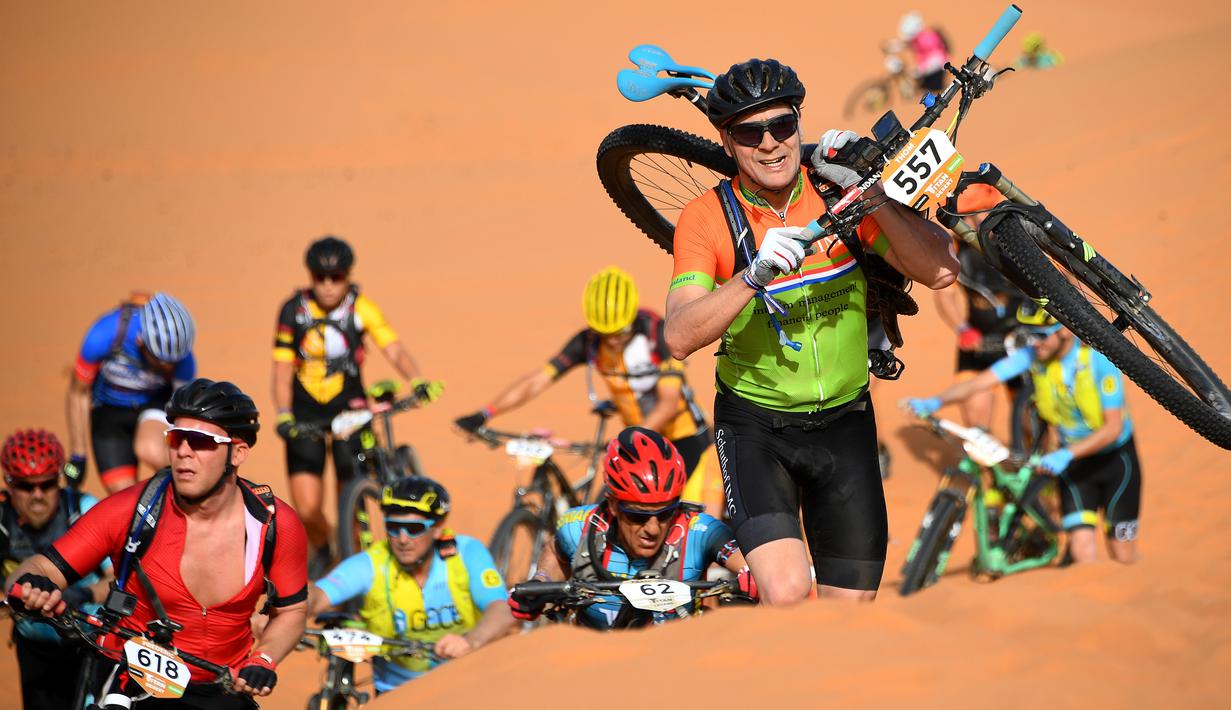 Para pebalap memanggul sepeda mereka menaiki gundukan pasir pada etape 1 edisi ke 14 balap sepeda gunung Titan Gurun 2019 di sekitar Kota Merzouga, Maroko, Minggu (28/4/2019). Trek Titan Gurun 2019 sepanjang 640 km menghubungkan antara Merzouga dan Maadid. (Franck Fife / AFP)