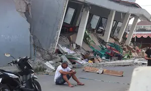 Seorang pria memeriksa ponselnya di dekat bangunan yang runtuh akibat gempa bumi di Reok, Provinsi Nusa Tenggara Timur, Indonesia, Minggu, 16 Agustus 2026. (Foto AP/Aquila Handayani Abbas)