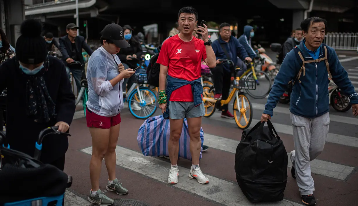 Seorang pria dan perempuan yang sedang berolahraga menggunakan smartphone mereka saat menunggu di persimpangan lampu merah selama jam sibuk di Beijing, China pada 14 Oktober 2020. (Photo by NICOLAS ASFOURI / AFP)