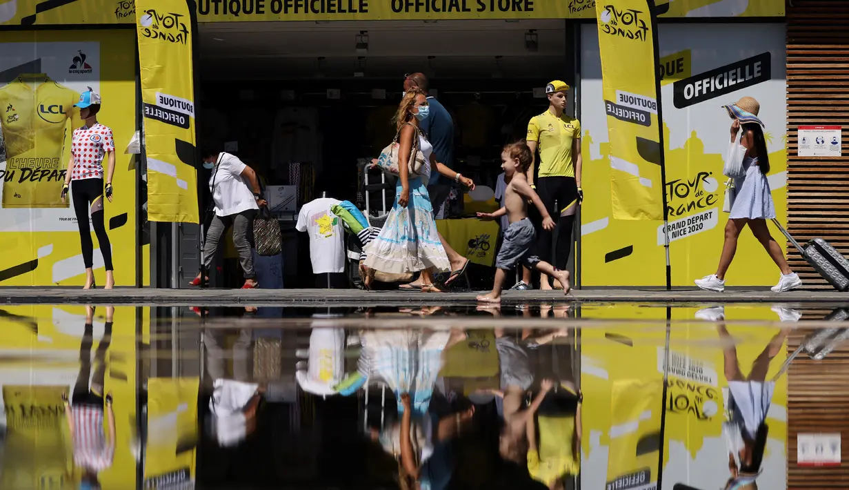 Orang-orang dengan masker melintasi toko resmi Tour de France 2020 di kota Nice, French Riviera, Rabu (26/8/2020). Ajang balap sepeda lintas kota di Prancis ini akan dimulai dari kota Nice pada 29 Agustus hingga 20 September di bawah bayang-bayang ‘gelombang kedua’ COVID-19. (Kenzo Tribouillard/AFP)