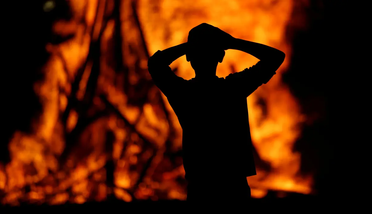 Seorang Yahudi Ultra-Ortodoks melihat kobaran api unggun selama perayaan Lag Ba-Omer di Shearim, Yerusalem, (25/5). Lag Ba-Omer merupakan hari libur Yahudi yang dirayakan pada hari ke-33 dari Penghitungan Omer. (REUTERS/Ronen Zvulun)