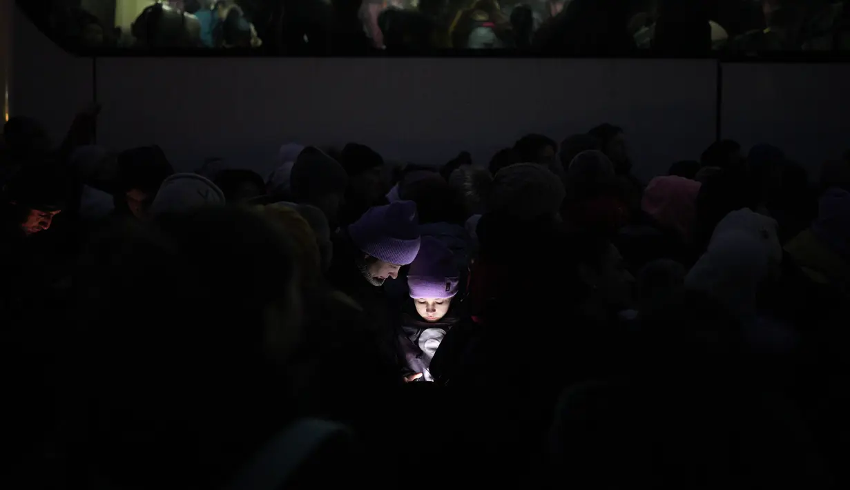 Wajah para pengungsi yang melarikan diri dari perang di Ukraina diterangi oleh cahaya dari smartphone saat mereka bergabung dengan garis mendekati perbatasan dengan Polandia di Shehyni, Ukraina, Minggu (6/3/2022). (AP Photo/Daniel Cole)