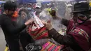 Seorang cenayang memberkati miniatur rumah dan uang palsu untuk seorang klien pada hari pembukaan Alasita Fair tahunan di El Alto, Bolivia, Selasa (24/1/2023). Barang- barang yang telah dibeli tidak dibawa pulang begitu saja. Ada cenayang yang mendoakan barang-barang tersebut dengan dupa dan bubuk khusus. (AP Photo/Juan Karita)