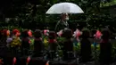Seorang pria dengan mengenakan payung melintasi patung Jizo (kiri) yang terlihat di Kuil Zojoji, Tokyo pada 22 Juni 2020. Jizo adalah pelindung dari anak-anak yang belum sempat lahir atau meninggal dalam kandungan dan saat masih bayi. (Photo by Philip FONG / AFP)
