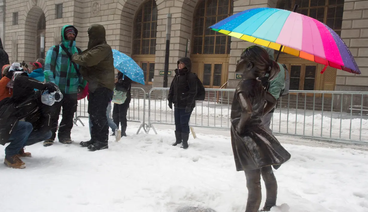 Warga mengambil gambar patung Fearless Girl memakai payung di New York, AS (14/3).  Badai salju menerjang kawasan Amerika Serikat timur laut, dari West Virginia hingga Maine, menyebabkan hujan salju lebat di sejumlah tempat. (AFP Photo/Don Emmert)