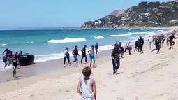 Seorang wanita melihat puluhan imigran yang menggunakan perahu karet berlarian menuju pantai Cadiz, Spanyol selatan, 9 Agustus 2017. Para imigran itu langsung berganti pakaian ketika tiba di daratan demi menghindari penangkapan polisi (Carlos Sanz via AP)