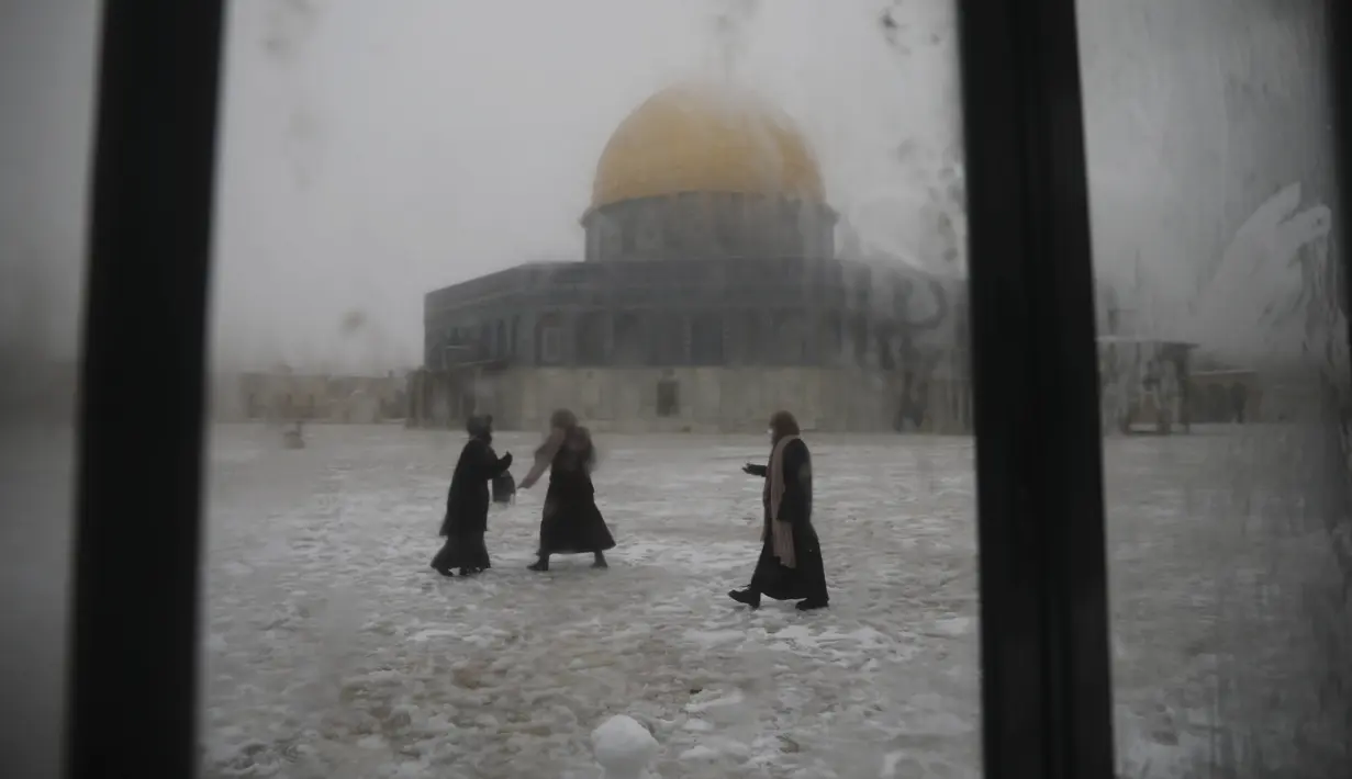 Para wanita bermain di salju dekat the Dome of the Rock atau Kubah Batu di kompleks Masjid Al Aqsa pada pagi bersalju di Kota Tua Yerusalem (18/2/2021). Pada 2013, badai salju besar terjadi di Yerusalem dan menyebabkan listrik mati di beberapa wilayah. (AP Photo/Mahmoud Illean)