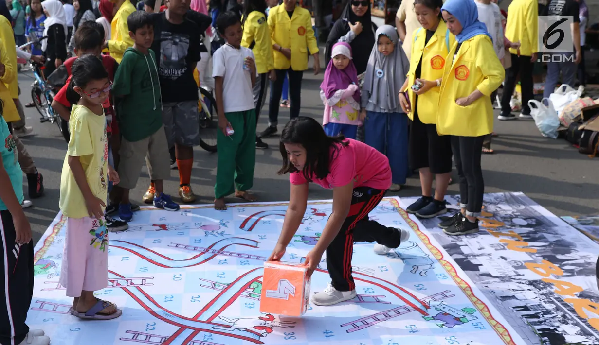 Mahasiswa jurusan Kriminologi Fisip UI mendampingi anak-anak bermain ular tangga saat gelaran Car Free Day di kawasan Bundaran HI, Jakarta, Minggu (18/11). Permainan ini bertujuan mengurangi anak-anak bermain gawai. (Liputan6.com/Helmi Fithriansyah)