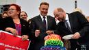 Pemimpin kelompok parlementer partai SPD, Thomas Oppermann (tengah) bersama Martin Schulz memotong kue pengantin dengan warna pelangi dan dihiasi patung-patung dua wanita dan dua pria di Bundestag di Berlin (30/6). (AFP Photo/Tobias Schwarz)
