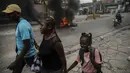 Orang-orang berjalan di sekitar ban yang dibakar oleh pengunjuk rasa untuk menuntut Perdana Menteri Haiti Ariel Henry mundur dan menyerukan kualitas hidup yang lebih baik, di Port-au-Prince, Haiti, Senin (29/8/2022). (AP Photo/Odelyn Joseph)