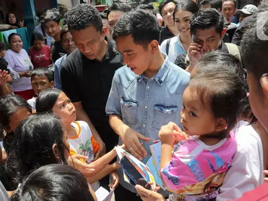 Calon wakil presiden nomor urut 2 Gibran Rakabuming Raka membagikan buku kepada anak-anak saat blusukan di kawasan Warakas, Jakarta, Selasa (16/1/2024). Gibran melakukan kegiatan tersebut dengan membagi buku dan berbincang dengan warga. (Liputan6.com/Herman Zakharia)