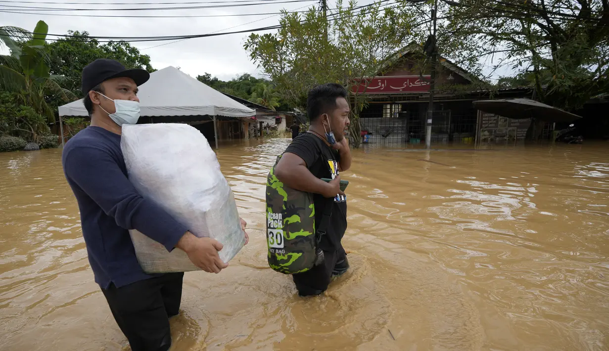 Warga membawa perbekalan kesehatan melalui jalan yang tergenang banjir di Hulu Langat, luar Kuala Lumpur, Malaysia, Minggu (19/12/2021). Banjir menyebabkan ribuan warga mengungsi dan banyak jalan yang memutus akses. (AP Photo/Vincent Thian)