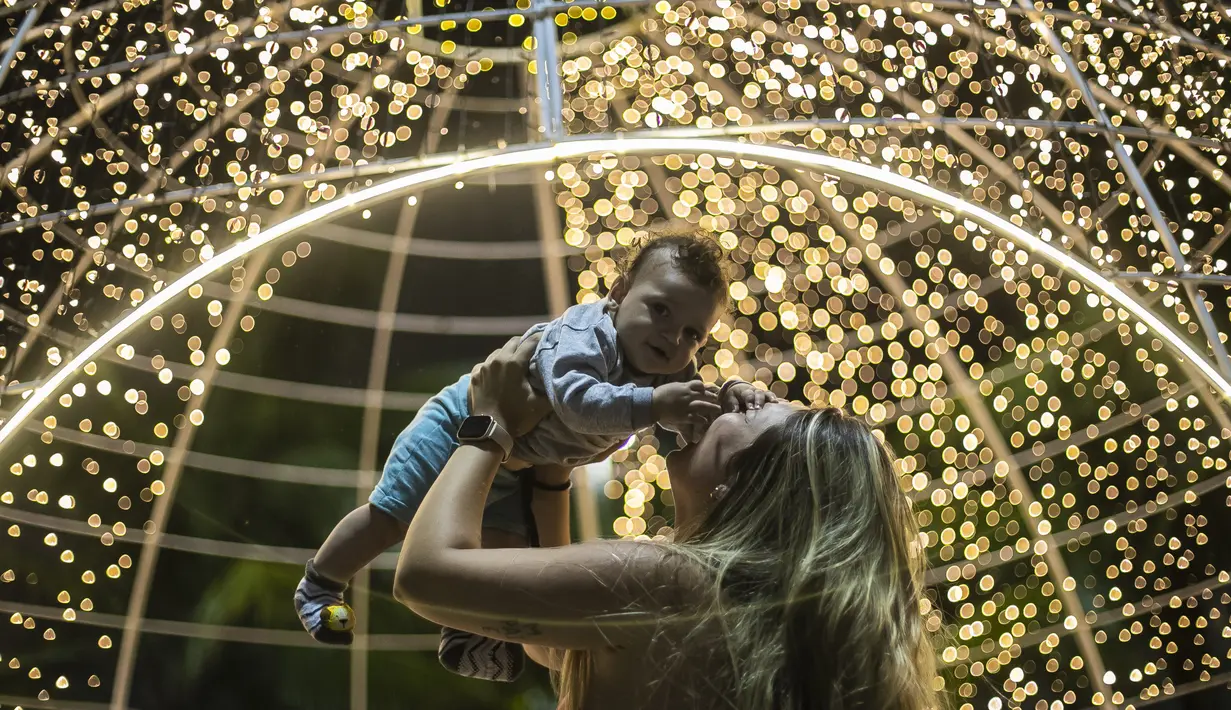 Seorang wanita mengangkat bayi di depan lampu jelang perayaan Natal di sepanjang pantai Copacabana, di Rio de Janeiro, Brasil (11/12/2021). Jelang perayaan Natal, taman dan pantai dihiasi lampu-lampu yang indah. (AP Photo/Bruna Prado)