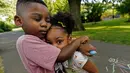 Zavion Guzman memeluk saudara perempuannya, Jazzmyn saat bermain di Belleville, New Jersey pada 30 Juni 2021. Lunisol Guzman mengadopsi keduanya saat masih bayi tetapi meninggal tahun lalu karena COVID-19 bersama pasangannya di awal gelombang pertama pandemi. (AP Photo/Mary Altaffer)