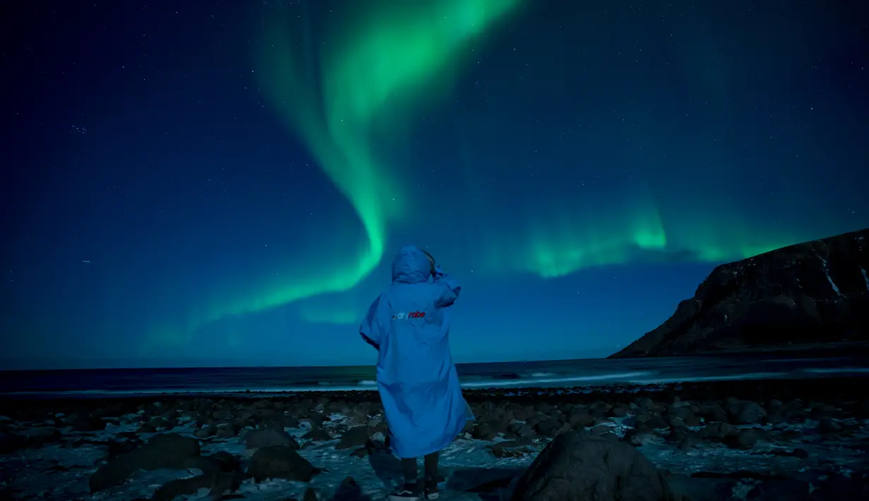Seseorang menonton fenomena alam Aurora Borealis atau Northern Lights di Unstad, lingkaran Arktik, Norwegia, Sabtu (3/3). Aurora menampilkan banyak warna, tapi yang sering muncul adalah hijau muda dan pink. (Olivier MORIN/AFP)