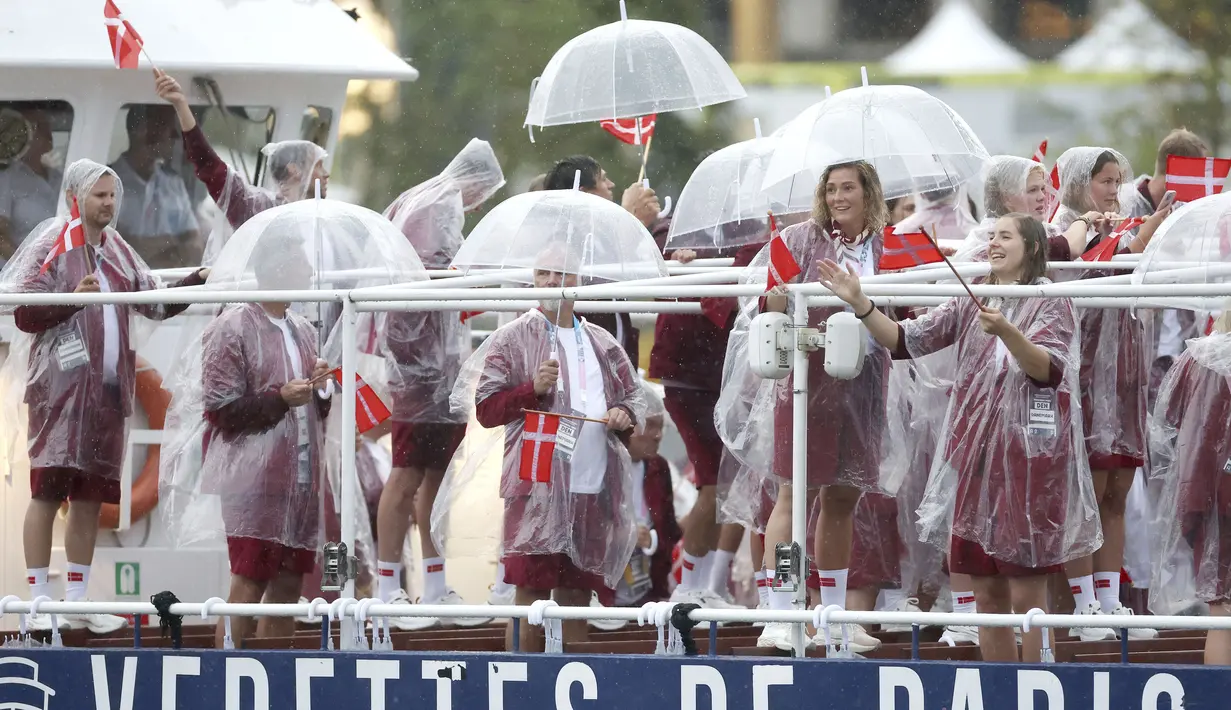 Atlet Denmark menggunakan payung dan jas hujan tetap bersemangat saat mengikuti parade acara pembukaan Olimpiade 2024 di Paris, Sabtu (27/7/2024). (Steph Chambers/Pool Photo via AP)