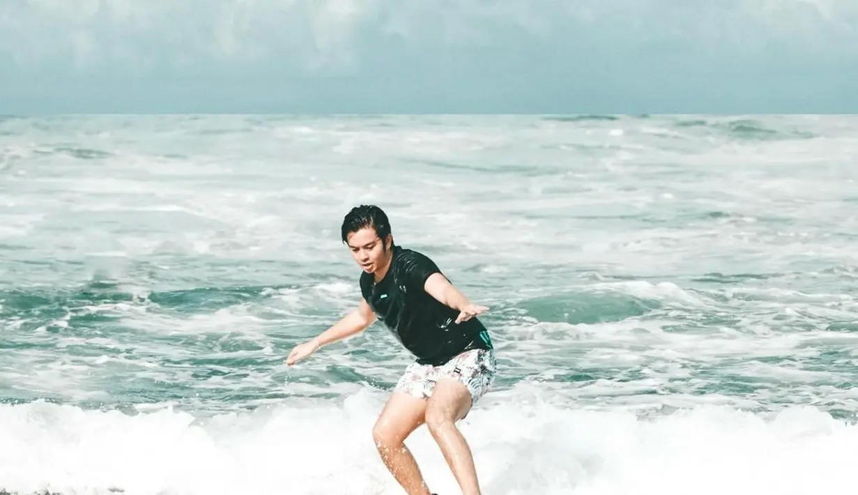 Inilah aksi Angga Yunanda saat menjajal berselancar di pantai. Meski pemula, pria 23 tahun ini bisa seimbang berdiri di papan selancar. (Liputan6.com/IG/@angga)