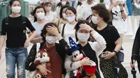 Pengunjung mengenakan masker guna melindungi diri dari virus corona berjalan menuju pintu masuk Tokyo Disneyland di Urayasu, dekat Tokyo, Rabu (1/7/2020). Tokyo Disneyland dibuka kembali untuk pertama kalinya dalam empat bulan setelah menangguhkan operasi karena kekhawatiran Covid-19. (AP/Koji Sasah