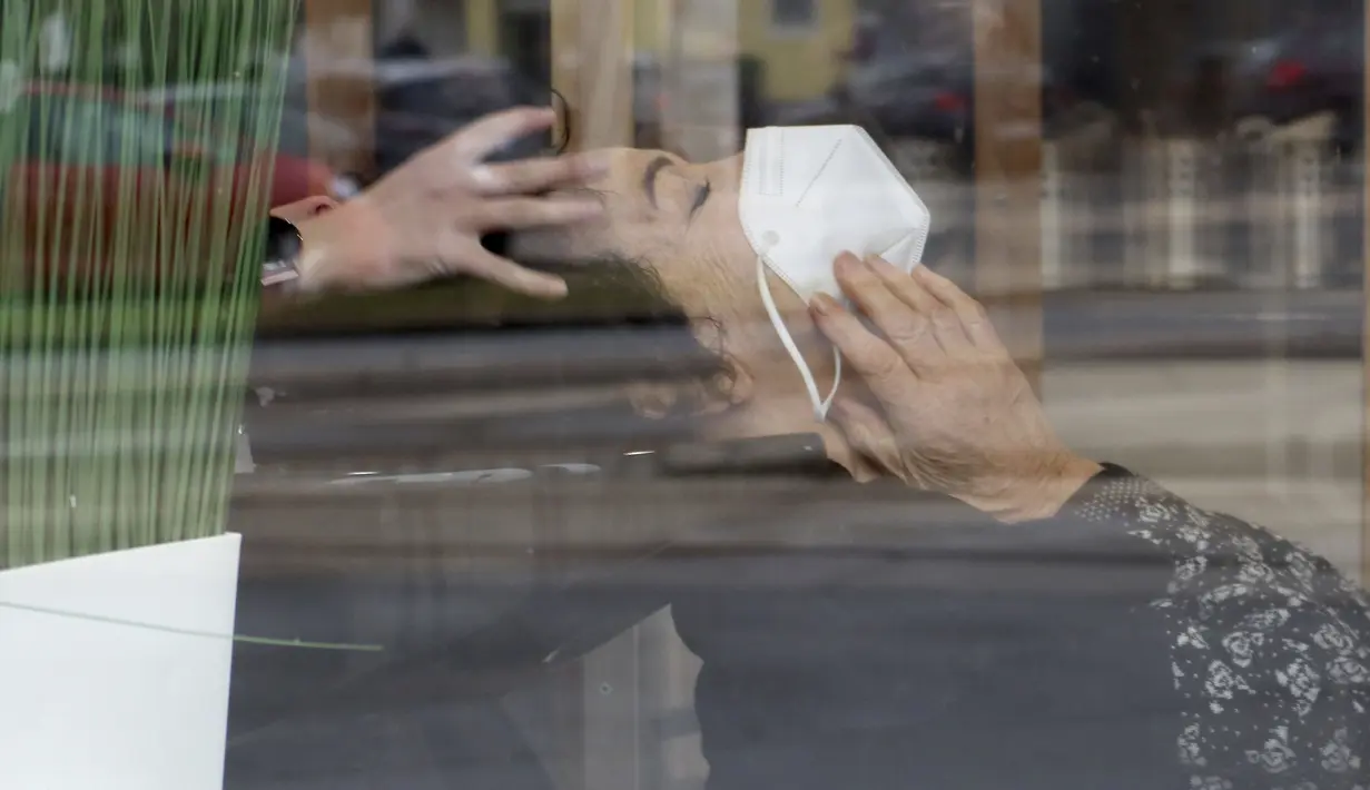 Terlihat dari kaca jendela, seorang perempuan dengan masker berada di salon rambut setelah pelonggaran lockdown di Wina, Austria, Senin (8/2/2021). Austria mulai melonggarkan lockdown covid-19 ketiga mereka dengan mengizinkan sekolah, museum dan toko dibuka kembali. (AP Photo/Ronald Zak)