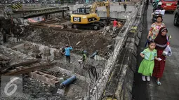 Sejumlah warga melintas di samping perbaikan jalan di kawasan Latumenten, Jakarta, Senin (05/12). Perbaikan jalan dengan mengganti pondasi baru tersebut guna memperkuat ketahanan badan jalan. (Liputan6.com/Faizal Fanani)