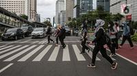 Para pekerja yang mengenakan masker menyeberang jalan di Jakarta, Rabu (2/2/2022). Kasus harian COVID-19 di Indonesia pada hari ini bertambah 17.895 jadi 94.109 kasus aktif, membuat total kasus sejak awal pandemi mencapai 4.387.286 kasus. (Liputan6.com/Faizal Fanani)