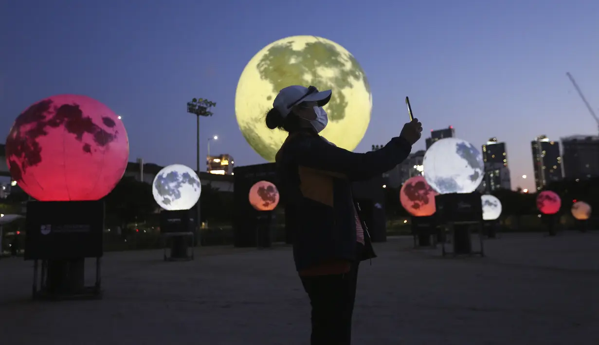 Warga berswafoto dekat instalasi bulan purnama yang bersinar di sebuah taman di Seoul, Korea Selatan, Jumat (18/9/2020). Pejabat setempat memasang bulan purnama buatan untuk meningkatkan semangat saat wabah COVID-19 sekaligus menyambut Chuseok, Thanksgiving versi Korea. (AP Photo/Ahn Young-joon)