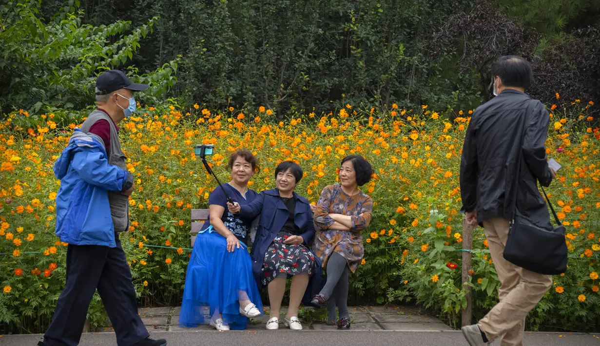 Wanita berpose selfie dengan bunga mekar di taman umum di Beijing, Sabtu (2/10/2021). Pengunjung memadati taman dan lokasi wisata di Beijing saat China merayakan hari kedua masa libur Hari Nasional. (AP Photo/Mark Schiefelbein)