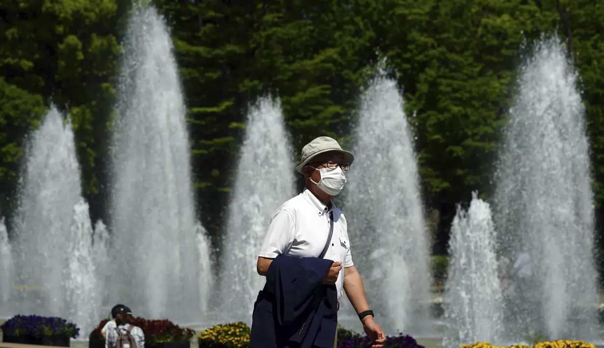 Seorang pria yang mengenakan masker pelindung untuk membantu mengekang penyebaran virus corona berjalan melalui taman di Tokyo (21/4/2021). Ibukota Jepang mengonfirmasi lebih dari 840 kasus virus corona baru pada hari Rabu. (AP Photo/Eugene Hoshiko)