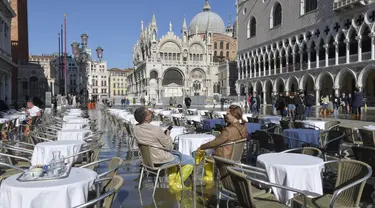 Orang-orang duduk di bar di St. Mark's Square yang terendam banjir di Venesia, Italia, Jumat (5/11/2021). Setelah Venesia mengalami banjir terparah kedua dalam sejarahnya pada November 2019, kota itu dibanjiri empat kali pasang luar biasa dalam waktu enam minggu. (AP Photo/Luigi Costantini)